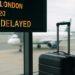 Pantalla de aeropuerto con vuelo retrasado y maleta junto a la puerta de embarque
